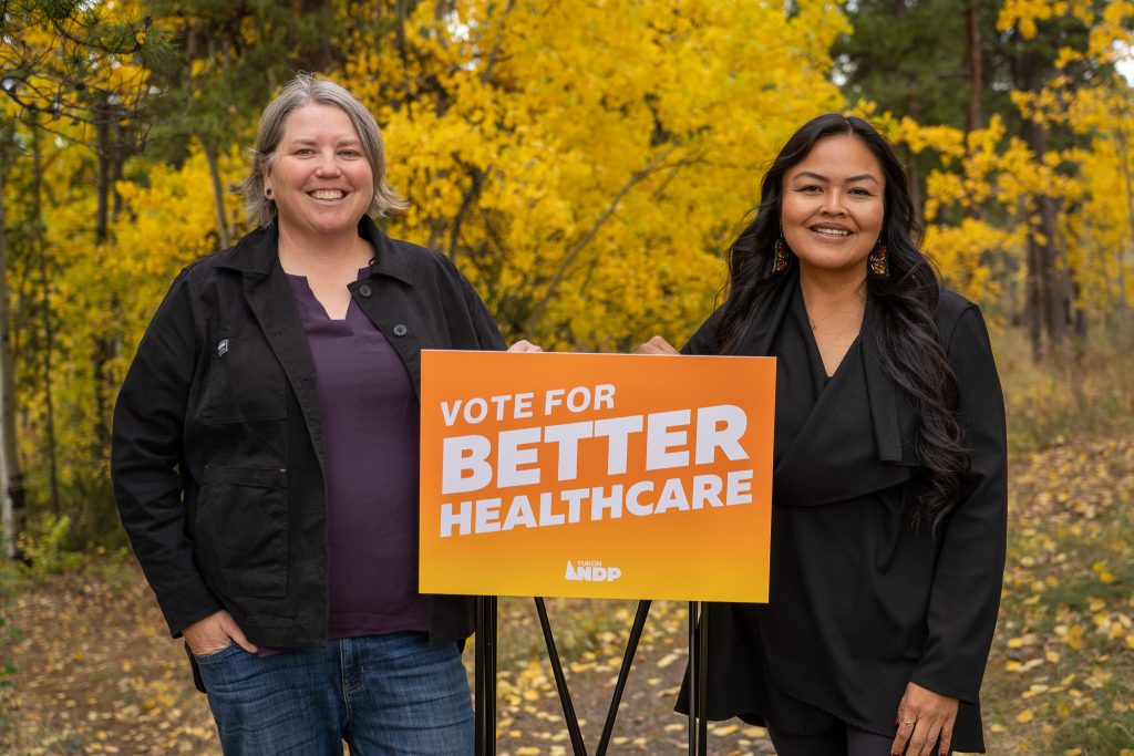 Kate White and Josie O'Brien stand in front of a "Vote for Better Healthcare" sign.